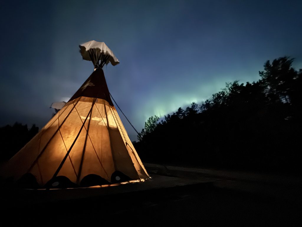 Indigenous tourism Saskatchewan: Teepee lit up at night with Northern Lights in the sky alternative view