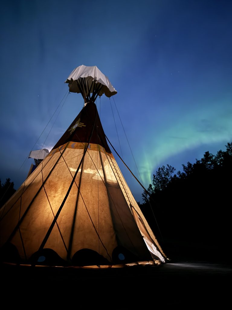 Indigenous tourism Saskatchewan: Teepee lit up at night with Northern Lights in the sky